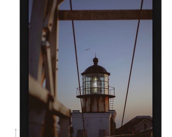 May include: A vintage lighthouse with a glowing light at dusk, framed by wooden beams and cables. The lighthouse is a white building with a black roof and a glass lantern. The sky is a soft blue with a hint of pink.