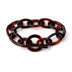 May include: A tortoiseshell-style link bracelet. The bracelet features large, oval-shaped links in shades of brown and amber. The clasp is a simple bar and circle design. The jewelry is displayed on a white background.