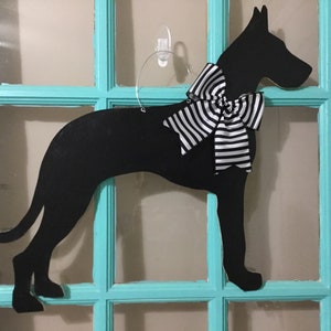 May include: Black silhouette of a dog with a large black and white striped bow, hanging on a teal door with glass panels.