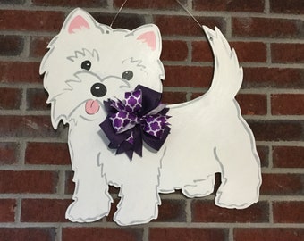 May include: White wooden cutout of a West Highland White Terrier dog with a purple and white bow. The dog is facing the left side of the image and has its tongue sticking out.