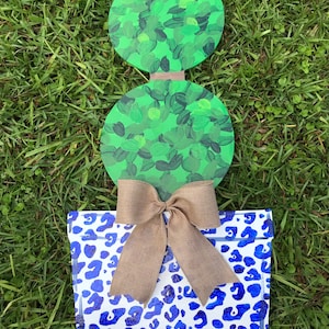 May include: A wooden topiary with two green round sections and a brown bow. The topiary is in a blue and white leopard print planter.