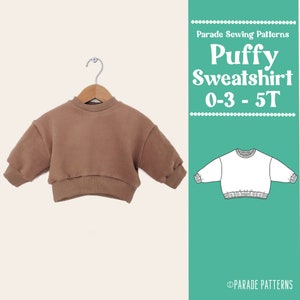 May include: A brown puffy sweatshirt for babies and toddlers. The sweatshirt has a round neckline and long sleeves. The pattern is for sizes 0-3 months to 5T. The text "Parade Sewing Patterns" and "Puffy Sweatshirt 0-3 - 5T" is on the right side of the image.