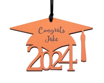 Może przedstawiać: Pomarańczowa drewniana ozdoba w kształcie czapki absolwenta z rokiem 2024 i tekstem "Congrats Jake" na niej.