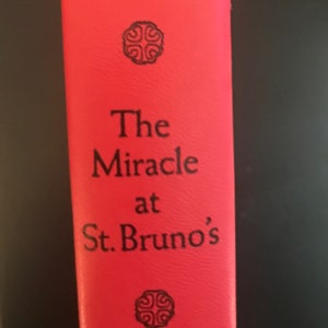May include: A red book with the title "The Miracle at St. Bruno's" by Philippa Carr. The book cover features a decorative design with a four-leaf clover.