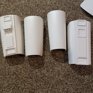 May include: Four white plastic pieces with different designs. The pieces are likely parts of a costume or prop.