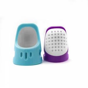 Pode incluir: Dois dedal para costura, um é azul claro e o outro é roxo com uma parte superior de malha branca.