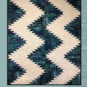 Puede incluir: Un patrón de colcha llamado "Pathways" diseñado por Villa Rosa Designs para Sugar Pine Quilt Designs. La colcha presenta un patrón geométrico de triángulos blancos y azules.