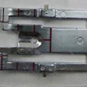 Puede incluir: Un pie de máquina de coser de plata con una guía de aguja de metal y un pequeño agujero en el centro. El pie tiene dos líneas rojas a cada lado.