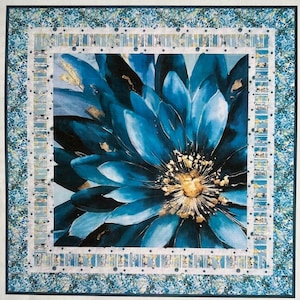 May include: A square quilt featuring a large, stylized blue flower with gold accents. The flower is the focal point, surrounded by a white border with a repeating pattern and a blue floral border. The quilt has a modern, artistic aesthetic.