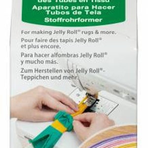 Puede incluir: Una herramienta Clover Fabric Tube Maker verde y blanca para hacer alfombras Jelly Roll y más. La herramienta se muestra en uso para crear un tubo de tela colorido. El empaque incluye el texto "Fabric Tube Maker" y "Jelly Roll" en varios idiomas.