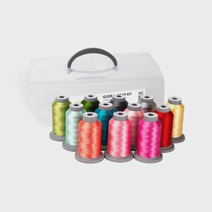 Puede incluir: Una caja de almacenamiento de plástico transparente con un asa negra contiene 12 carretes de hilo de colores. Los colores del hilo incluyen amarillo, turquesa, rojo, rosa y verde. La caja está etiquetada como "GLIDE Thread Kit".