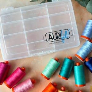 May include: A clear plastic storage box with multiple compartments for organising small items. The box has a label that reads "Aurifil Every Stitch Counts". The box is surrounded by spools of colourful thread.