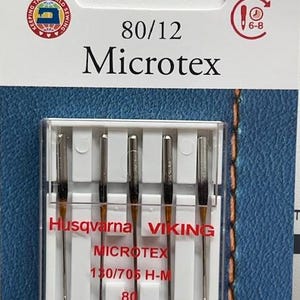 Puede incluir: Un paquete de agujas para máquina de coser Husqvarna Viking Microtex. El paquete es blanco y rojo, con el texto "80/12 Microtex" y "130/705 H-M 80". El paquete contiene cinco agujas finas.
