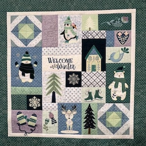 May include: A winter-themed quilt with various appliqued designs. The quilt features a snowman, penguin, bear, deer, and other winter motifs. The text "WELCOME WINTER" is prominently displayed. The color palette includes blues, greens, and whites.