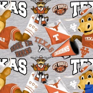 Może przedstawiać: Wzór tkaniny w kolorze szarym i pomarańczowym z powtarzającym się motywem kreskówkowej maskotki w stroju piłkarskim trzymającej piłkę nożną. Maskotka to byk z dużą głową i rogami. Wzór zawiera również słowa "Texas Longhorns" i "Hook 'em Horns".