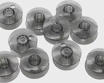 May include: A collection of ten clear plastic sewing machine bobbins. Each bobbin has a circular shape with a central hole and a transparent, rounded exterior. The bobbins are arranged on a light gray background.