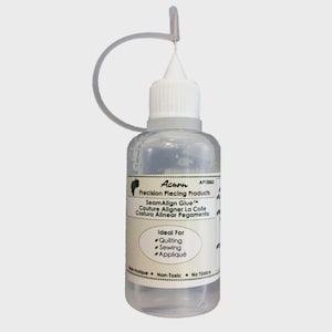 Könnte beinhalten: Klare Flasche Acorn SeamAlign Kleber zum Quilten, Nähen und Applizieren. Die Flasche hat einen weißen Deckel und ein Etikett mit Text in Englisch, Französisch und Spanisch. Der Kleber ist ungiftig.