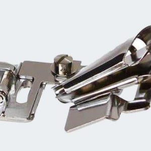 May include: A silver sewing machine foot attachment for creating rolled hems. The foot has a curved metal tube and a metal plate with a screw.