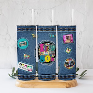 Puede incluir: Tres vasos de acero inoxidable con un patrón de mezclilla y gráficos con temática de los 80. Los gráficos incluyen una cinta de casete, patines, una computadora, una grabadora de casetes y un corazón con el texto "Me encanta la década de los 80".