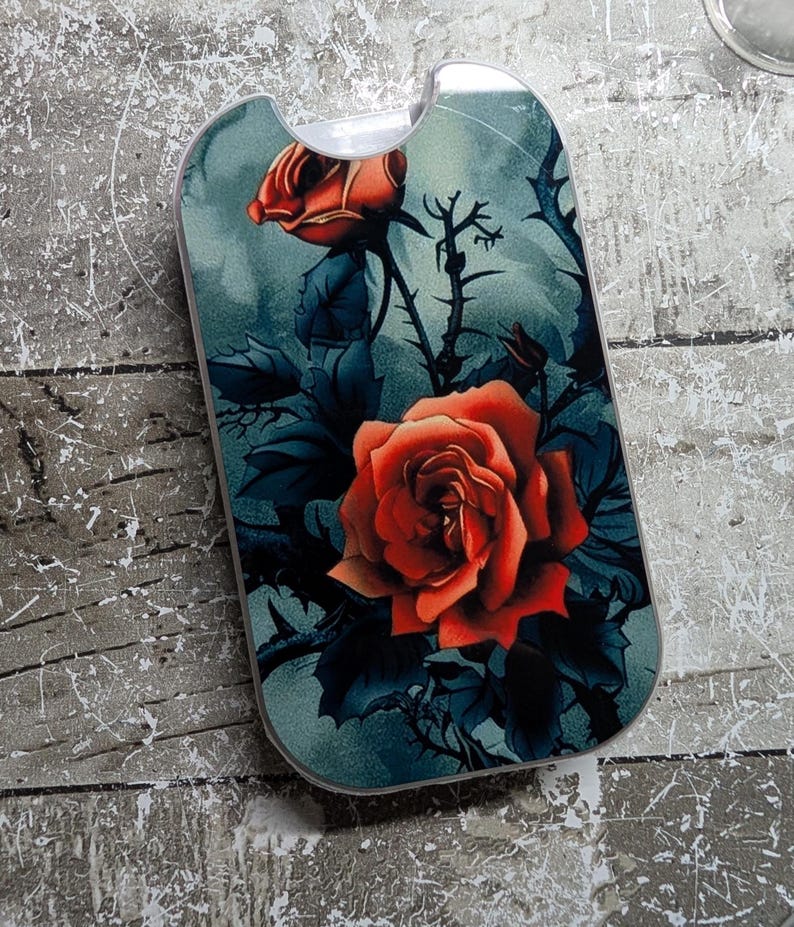 May include: A phone case featuring a vibrant red rose design against a teal background. The case has a curved top and a dark floral pattern with thorns and leaves. The rose is the focal point, with detailed petals.
