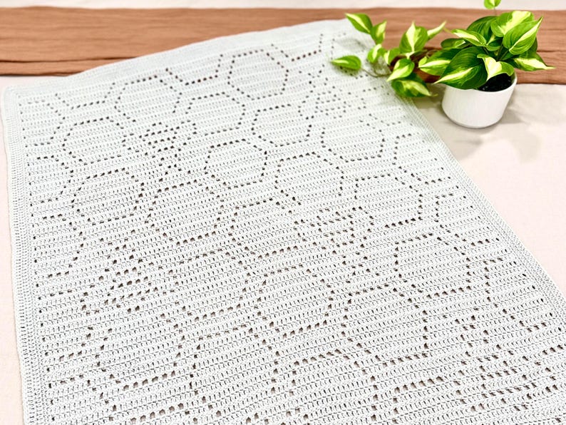 May include: A white crocheted blanket with a geometric pattern. The blanket is made with a delicate openwork stitch, creating a lacy effect.