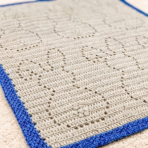 May include: A crocheted blanket with a beige background and a blue border. The blanket has a diamond pattern.