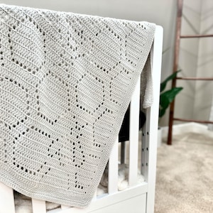 May include: A gray crocheted baby blanket with a diamond pattern, draped over a white crib.