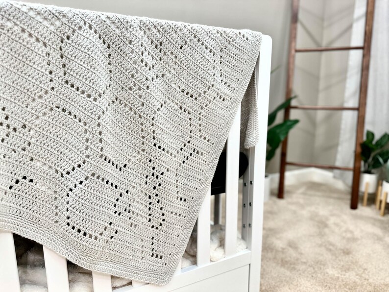 May include: A gray crocheted baby blanket with a diamond pattern, draped over a white crib.