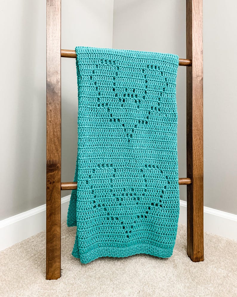 a blue crocheted blanket sitting on top of a wooden ladder