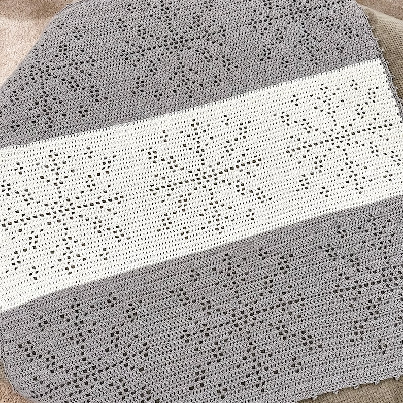 a snowflake filet crocheted baby blanket laying on top of an ottoman
