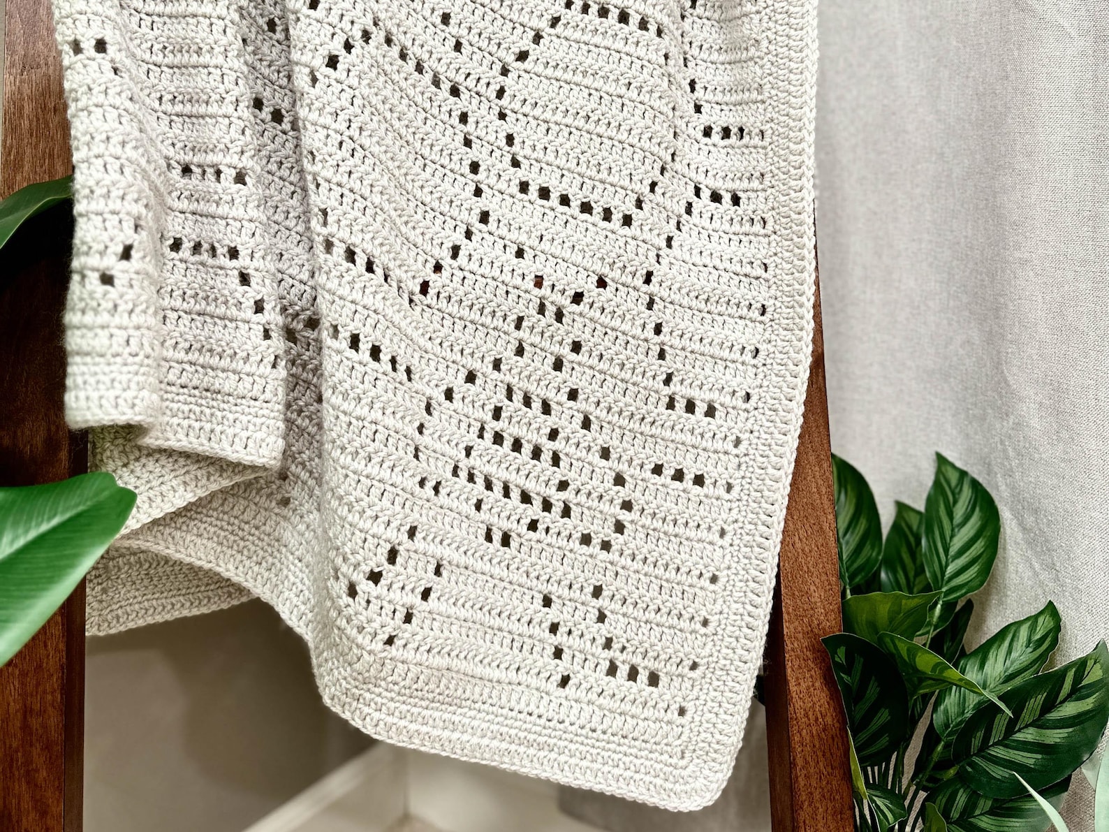 Filet crochet baby blanket draped over a wooden ladder, featuring a bee motif in soft neutral yarn