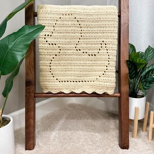 Handmade filet crochet baby blanket, with a rubber duck design and scallop border. Blanket is folded to view a single duck and draped over a wooden blanket ladder.