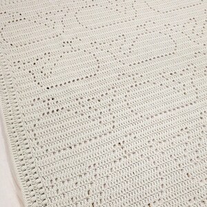 May include: A light gray crocheted blanket with a repeating heart pattern. The blanket is made of soft yarn and has a textured appearance. The edges are finished with a decorative border, adding a touch of elegance to the handmade item.