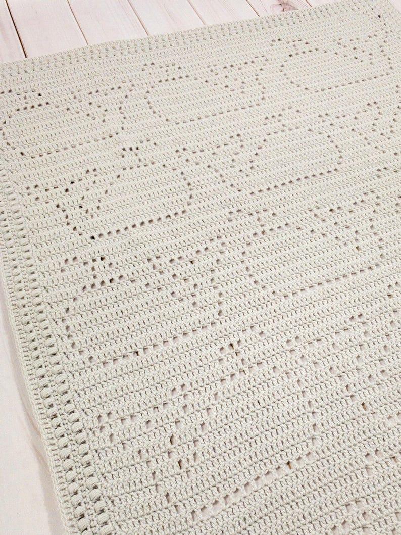 May include: A light gray crocheted blanket with a repeating heart pattern. The blanket is made of soft yarn and has a textured appearance. The edges are finished with a decorative border, adding a touch of elegance to the handmade item.
