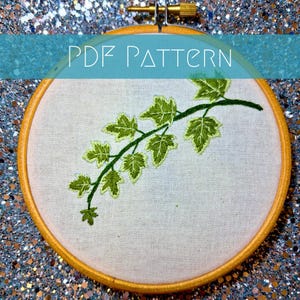 K&ouml;nnte beinhalten: Ein runder Stickrahmen aus Holz mit wei&szlig;em Stoff, der ein handgesticktes Motiv einer gr&uuml;nen Efeuranke mit detaillierten Bl&auml;ttern zeigt. Der Text PDF PATTERN ist in Wei&szlig; &uuml;ber die Mitte des Bildes auf den Stickrahmen gedruckt.