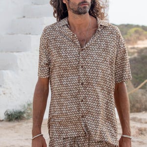 May include: A short-sleeved button-down shirt and matching shorts set. The shirt and shorts feature a woven pattern in shades of brown and tan. The model is wearing a silver bracelet and necklace.