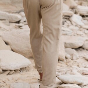May include: A pair of beige linen trousers with a drawstring waistband. The trousers are cuffed at the ankles and have a relaxed fit.