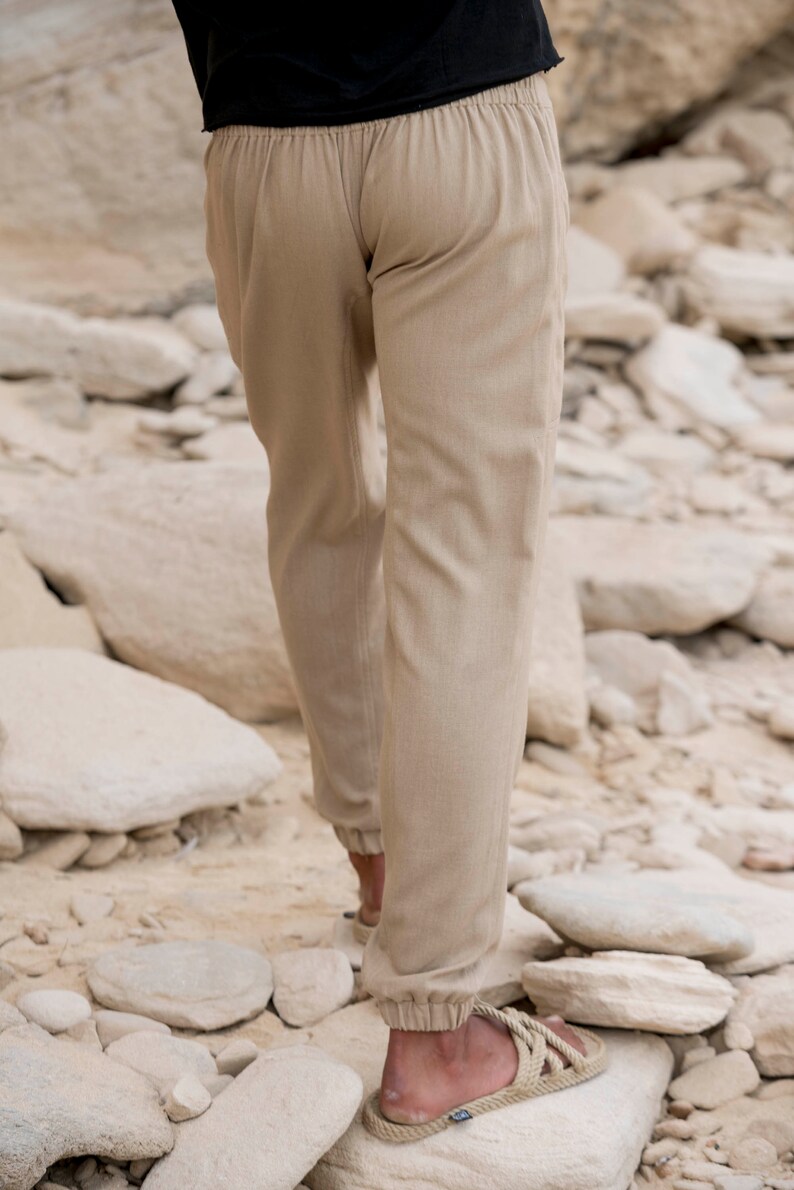 May include: A pair of beige linen trousers with a drawstring waistband. The trousers are cuffed at the ankles and have a relaxed fit.