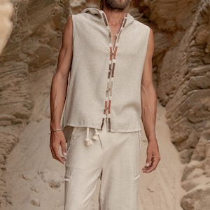 May include: A sleeveless hooded top with a beige linen fabric and a brown and beige trim. The top has a drawstring closure at the neck. The model is wearing beige linen shorts.