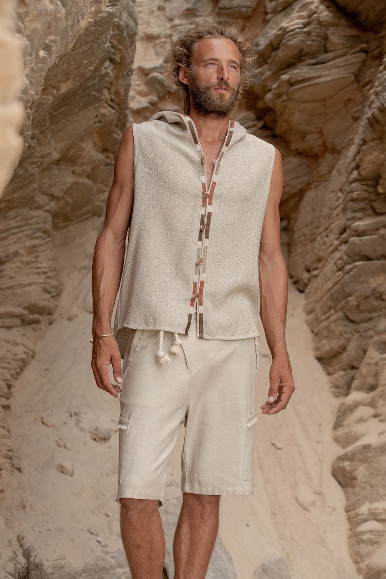 May include: A sleeveless hooded top with a beige linen fabric and a brown and beige trim. The top has a drawstring closure at the neck. The model is wearing beige linen shorts.