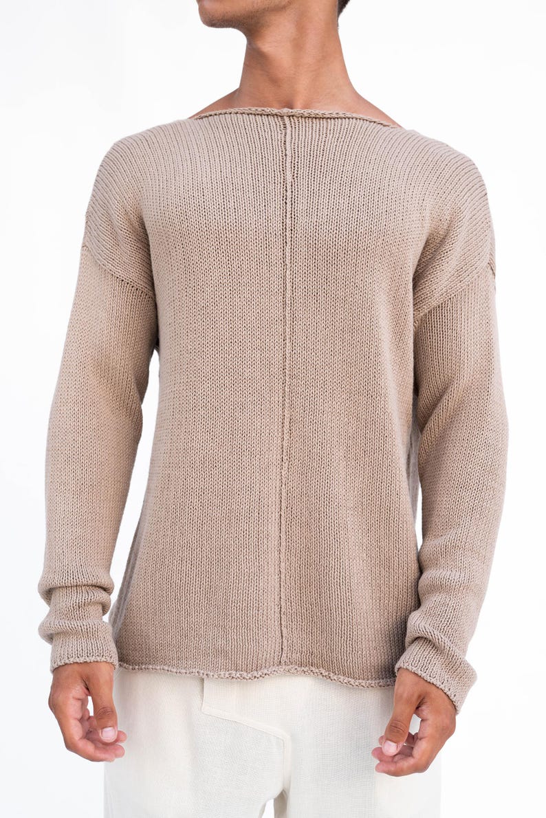 May include: A beige knitted sweater with a boat neck and long sleeves. The sweater has a vertical seam down the back. The sleeves end with ribbed cuffs. The sweater is made of a soft, textured material.