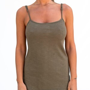 Op de afbeelding: Een vrouw draagt een lange, olijfgroene, mouwloze tanktop met dunne bandjes. De top heeft een losse pasvorm en een iets langere lengte.