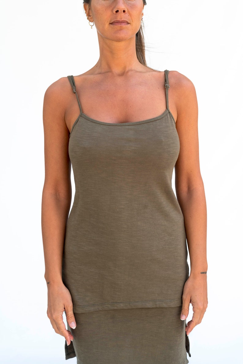 Op de afbeelding: Een vrouw draagt een lange, olijfgroene, mouwloze tanktop met dunne bandjes. De top heeft een losse pasvorm en een iets langere lengte.