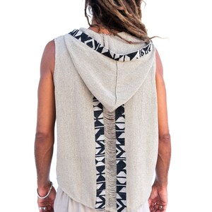 Op de afbeelding: Een sleeveless hooded vest met een zwart-wit geometrisch patroon op de rug. Het vest is gemaakt van een licht beige stof.