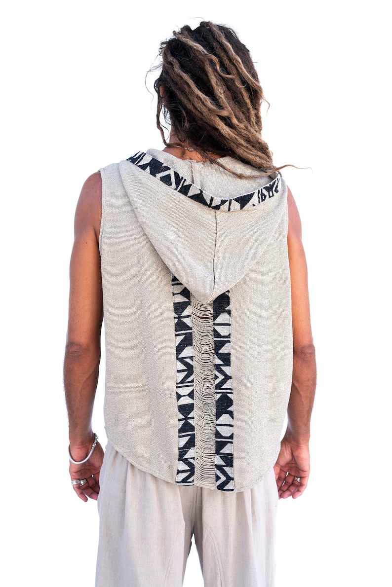 Op de afbeelding: Een sleeveless hooded vest met een zwart-wit geometrisch patroon op de rug. Het vest is gemaakt van een licht beige stof.