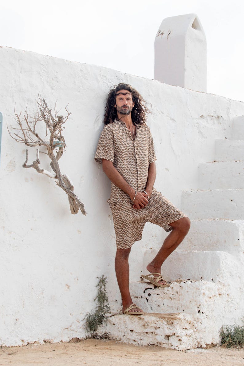 May include: A matching beige patterned shirt and shorts set. The short-sleeved button-down shirt and shorts have a repeating geometric design. The person is wearing sandals and standing on white steps.