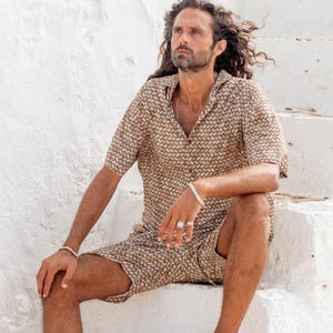 May include: A matching two-piece set featuring a short-sleeved button-down shirt and shorts. The set has a woven pattern in shades of brown and tan. The person is wearing rope sandals and silver jewelry. The outfit is suitable for warm weather.