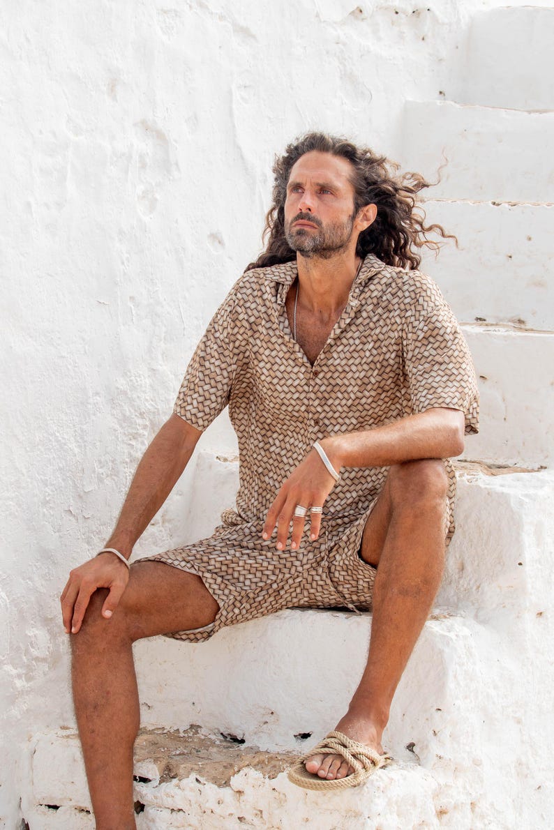 May include: A matching two-piece set featuring a short-sleeved button-down shirt and shorts. The set has a woven pattern in shades of brown and tan. The person is wearing rope sandals and silver jewelry. The outfit is suitable for warm weather.