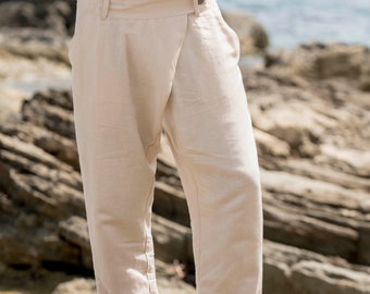 Op de afbeelding: Off-white broek met een wikkelstijl sluiting aan de voorzijde, voorzien van een enkele knoop bij de tailleband, zijzakken en een rechte pijp. De broek heeft een zichtbare naad die over de voorkant van elke broekspijp loopt en een zoom.