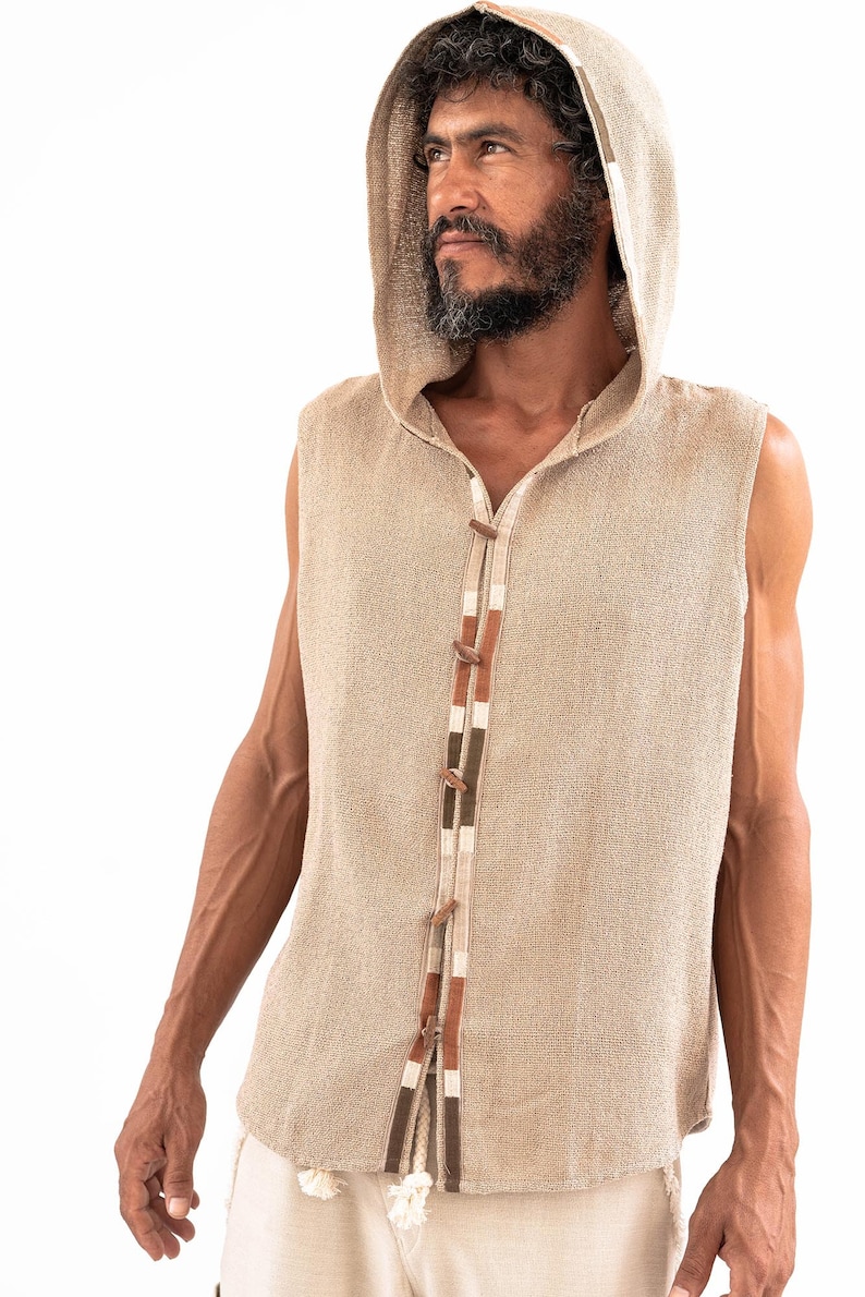 May include: A sleeveless hooded vest with a beige linen fabric and a brown, white, and green trim. The vest has a button closure and a rope tie at the bottom.
